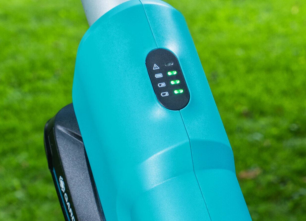 Zbliżenie na niebieski element urządzenia z czarnym panelem i zielonymi diodami. W tle widoczna jest trawa.