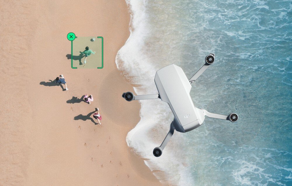 Na plaży widać trzy osoby oraz drona unoszącego się nad nimi. Dron jest biały, a na piasku widoczne są ślady stóp.