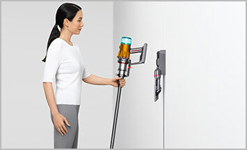 Widok osoby odwieszającej odkurzacz na ścienną stację ładującą