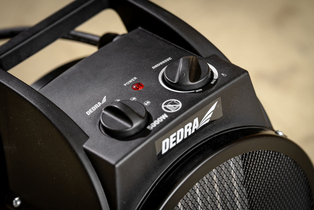 Czarna nagrzewnica elektryczna z widocznymi pokrętłami i czerwonym wskaźnikiem. Na urządzeniu znajduje się logo \'DEDRA\' oraz oznaczenie \'5000W\'.
