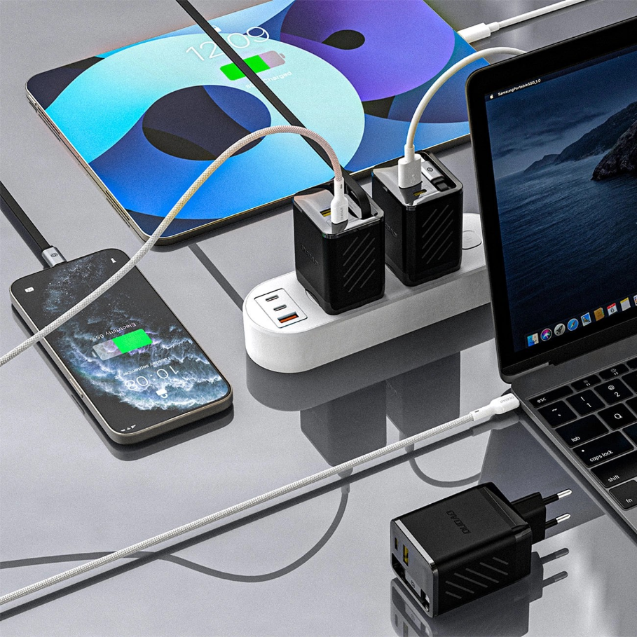 Na obrazie widać kilka urządzeń elektronicznych podłączonych do ładowarki sieciowej z kilkoma portami USB. Na ekranach urządzeń widoczne są ikony ładowania baterii.