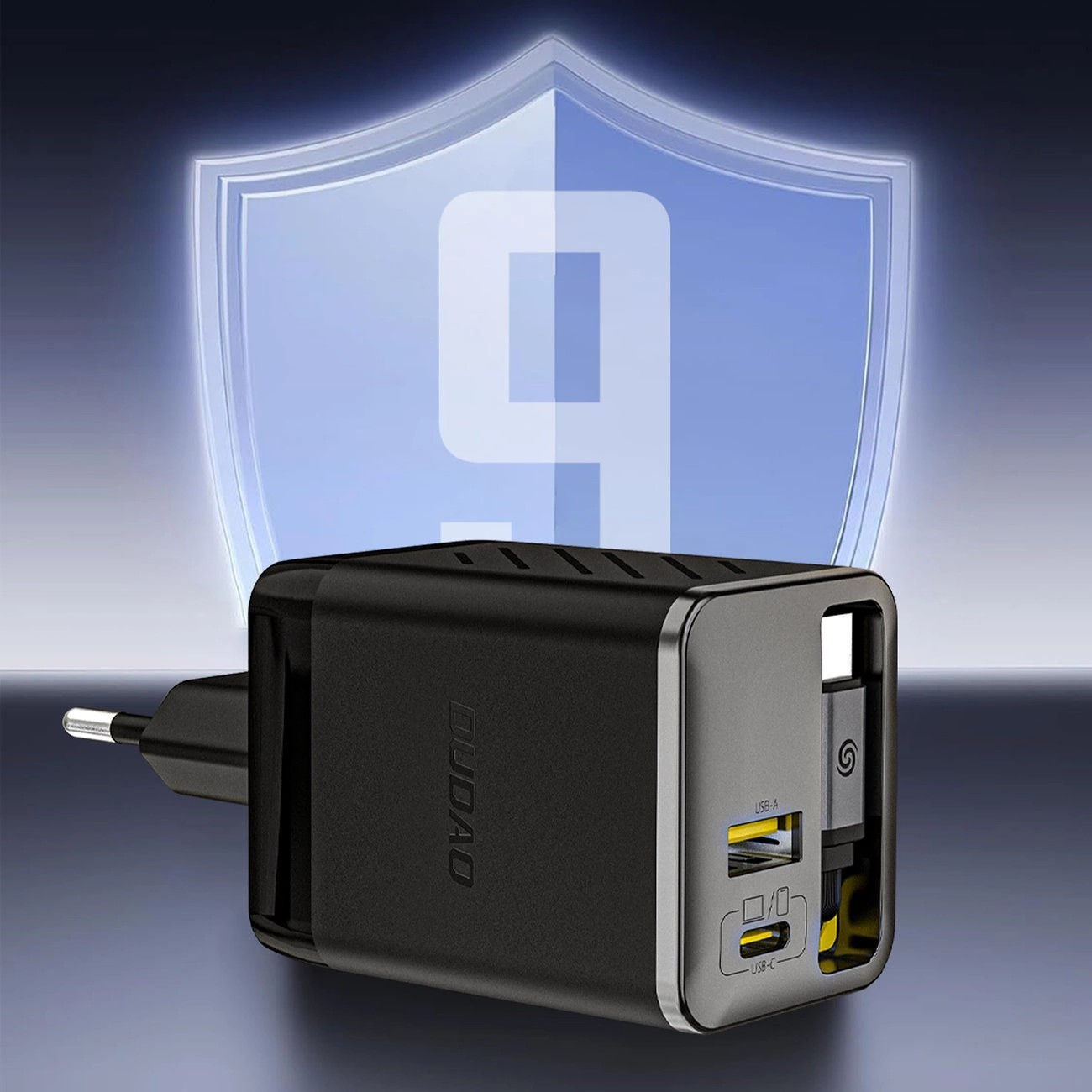 Czarna ładowarka sieciowa z wbudowanym zwijanym kablem USB-C, posiada dwa porty USB oznaczone jako USB-A i USB-C. W tle widoczna jest niebieska tarcza z dużą cyfrą 9.