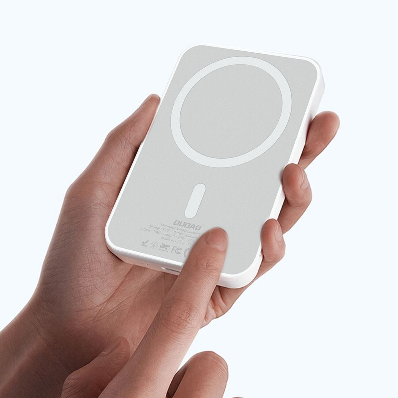 Osoba trzyma biały powerbank z okrągłym wzorem na powierzchni i logo \'DUDAO\' widocznym na dole urządzenia.
