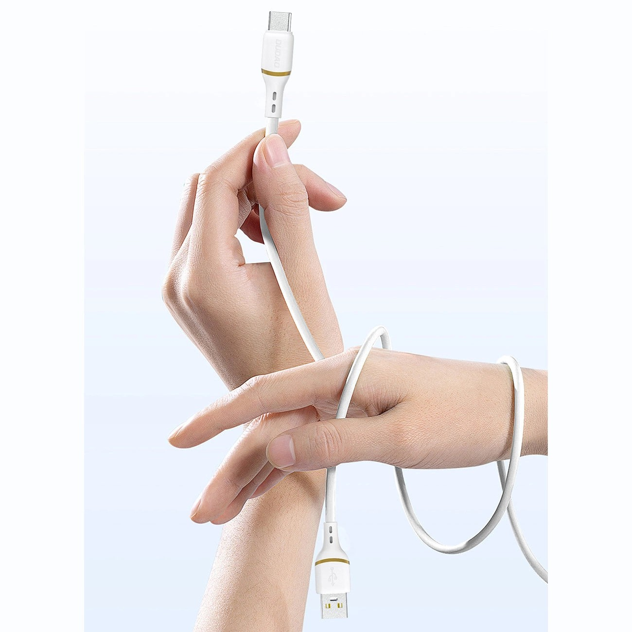 Na zdjęciu widoczny jest biały kabel USB-C z silikonową powłoką, trzymany przez dwie dłonie. Na wtyczce znajduje się napis \'dudao\'.