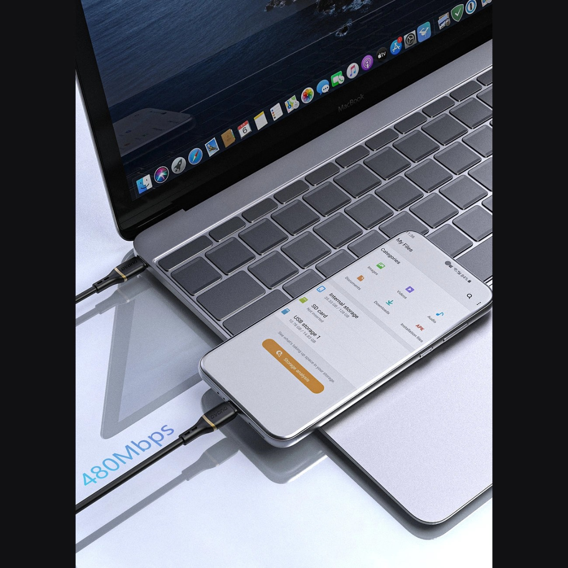 Na obrazie widać laptopa z otwartym ekranem i klawiaturą, do którego podłączony jest smartfon za pomocą kabla USB-C. Na ekranie smartfona widoczny jest interfejs aplikacji z różnymi opcjami, a obok kabla znajduje się napis \'480Mbps\'.