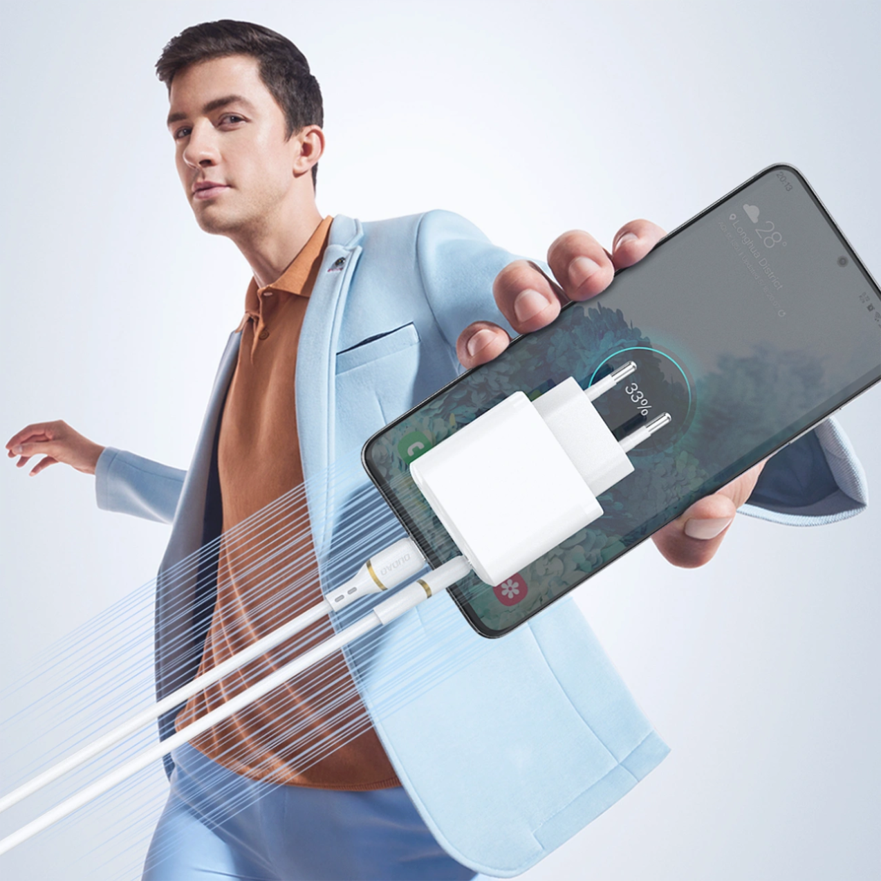Osoba w jasnym garniturze trzyma smartfon z podłączonym białym kablem USB-C, na ekranie widoczny jest wskaźnik ładowania na poziomie 33%.