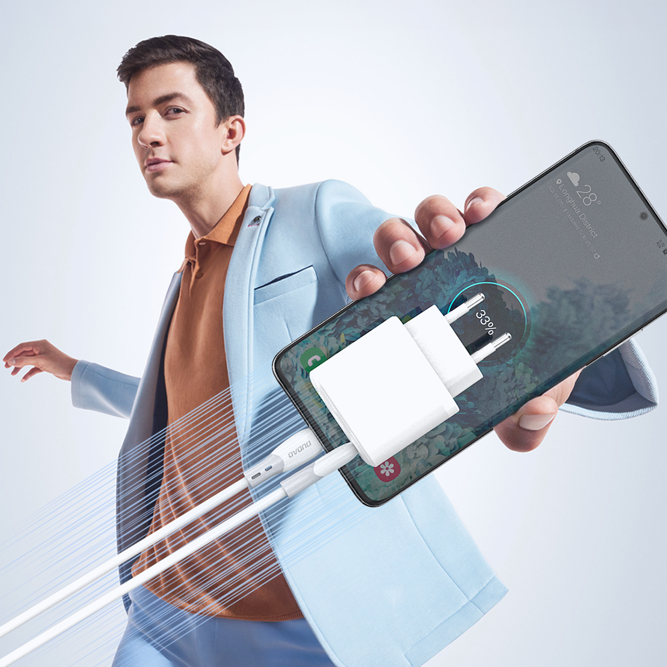 Osoba w jasnym garniturze trzyma smartfon z podłączonym białym kablem USB-C. Na ekranie telefonu widoczny jest wskaźnik ładowania na poziomie 33%.
