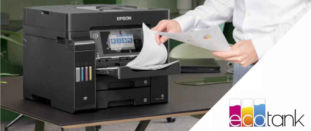 Na stole znajduje się czarne urządzenie wielofunkcyjne z logo EPSON, z którego osoba wyciąga wydrukowane kartki. Obok widoczne jest kolorowe logo ecotank.