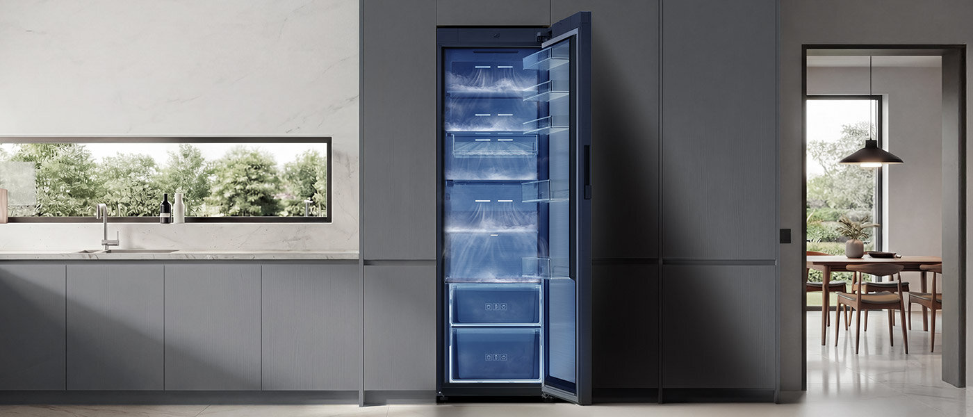 Chłodziarka z systemem All Around Cooling W nowoczesnej kuchni znajduje się otwarta lodówka z niebieskim wnętrzem i kilkoma półkami. W tle widać duże okno z widokiem na zieleń oraz stół z krzesłami.