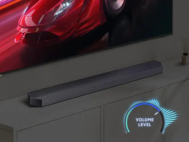 Soundbar Samsung HW-Q990H pod telewizorem z czerwonym samochodem i świecącym niebieskim wskaźnikiem głośności.