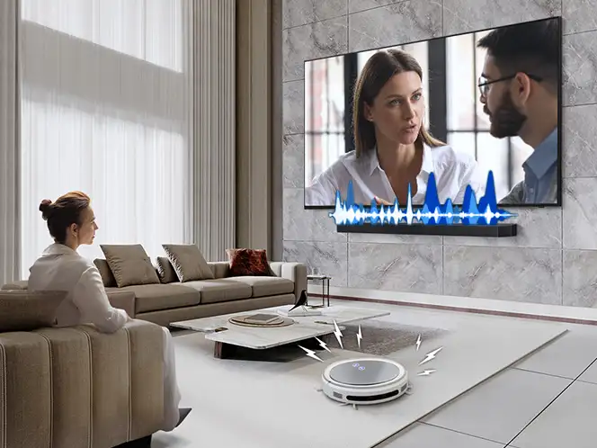 Kobieta ogląda rozmowę na telewizorze z soundbarem Samsung HW-Q990H, obok robota sprzątającego i niebieskich fal dźwięku.