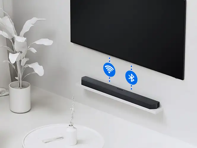 2026-hw-q990h-wireless-tv-connection 664x498 Czarny soundbar Samsung HW-Q990H pod czarnym telewizorem z niebieskimi ikonami Wi-Fi i Bluetooth w białym wnętrzu.