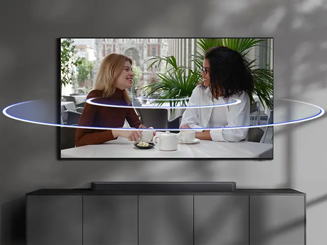 Dwie kobiety rozmawiające przy stole na ekranie telewizora z jasnymi poziomymi liniami dźwięku wokół.