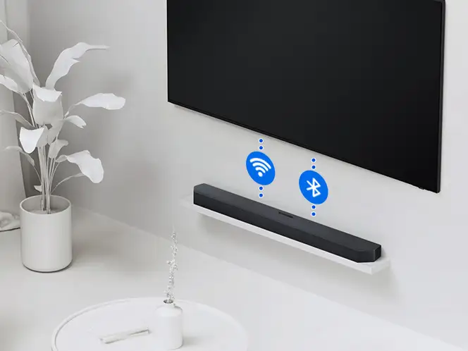 2026-hw-q930h-wireless-tv-connection 664x498 Czarny soundbar Samsung HW-Q930H pod czarnym telewizorem z niebieskimi ikonami Wi-Fi i Bluetooth w białym wnętrzu.