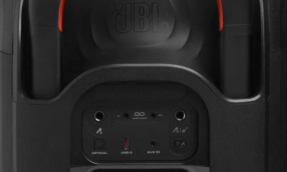 Czarny panel z logo JBL zawiera różne porty: Optical, USB-C, AUX IN oraz przyciski i wskaźniki. Widać także czerwone akcenty na górnej części urządzenia.