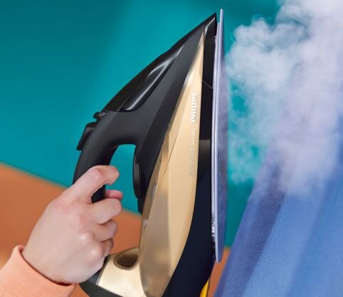 Osoba trzyma żelazko, z którego wydobywa się para, a na obudowie widoczny jest napis \'philips\'.
