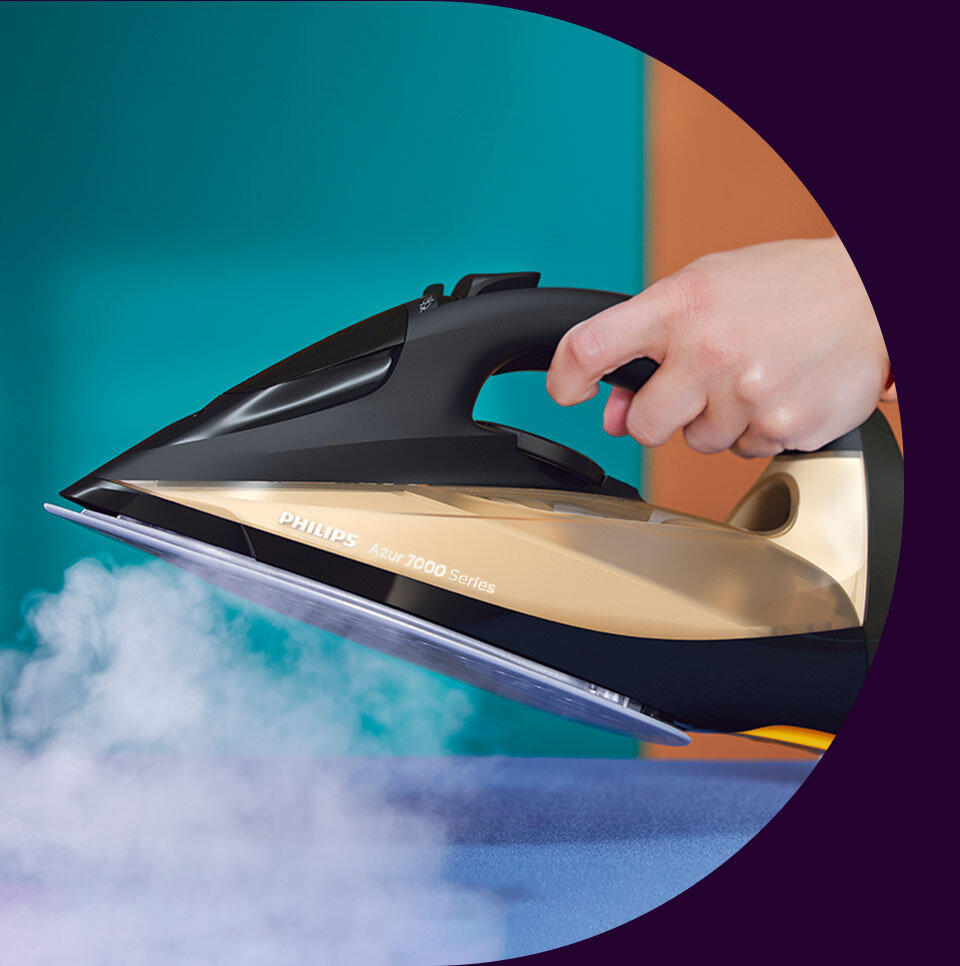 Osoba trzyma żelazko w kolorze czarno-złotym, z którego wydobywa się para. Na żelazku widoczny jest napis \'PHILIPS Azur 7000 Series\'.