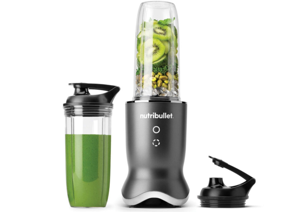 Na obrazie widoczny jest blender personalny z logo \'nutribullet\', wypełniony składnikami takimi jak kiwi i orzechy. Obok znajduje się pojemnik z zielonym napojem oraz dodatkowa pokrywka.