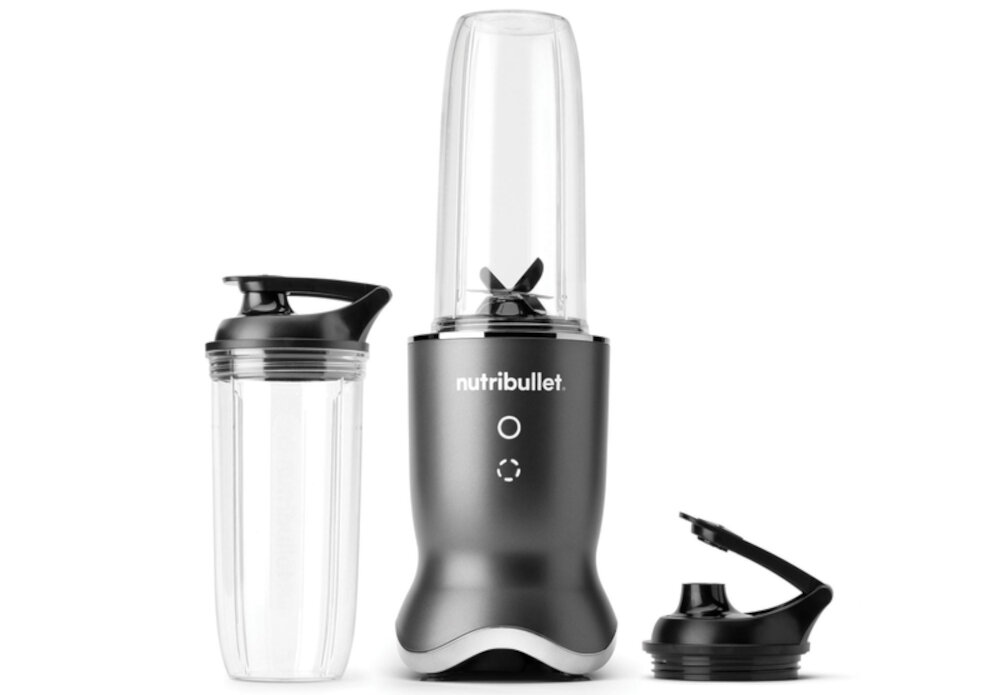 Na obrazie widoczny jest blender personalny z logo \'nutribullet\' na korpusie, obok znajduje się dodatkowy pojemnik z pokrywką oraz osobna pokrywka. Blender ma ciemny korpus i przezroczysty pojemnik z ostrzami wewnątrz.