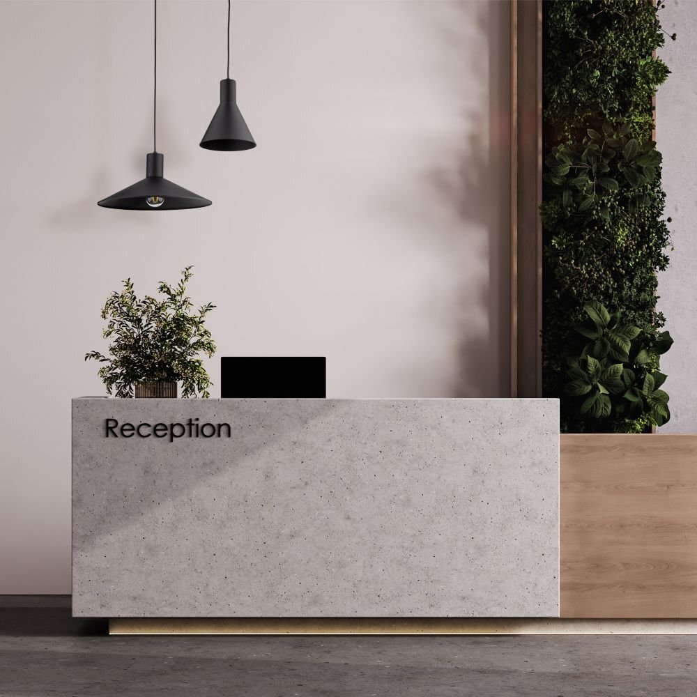 Na zdjęciu znajduje się nowoczesna recepcja z betonowym blatem, na którym widnieje napis \'Reception\', oraz dwie czarne lampy wiszące nad blatem. Obok recepcji znajduje się ściana z roślinnością.