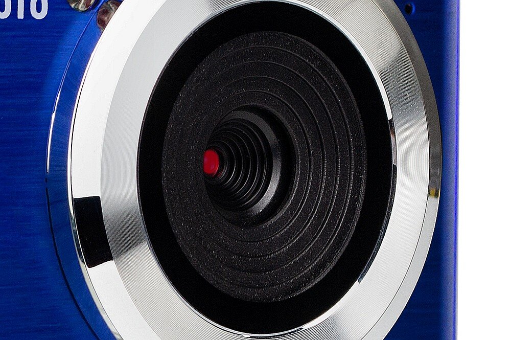 Zbliżenie na obiektyw aparatu z metalicznym pierścieniem i czarnym wnętrzem. W tle widoczny jest niebieski kolor obudowy.