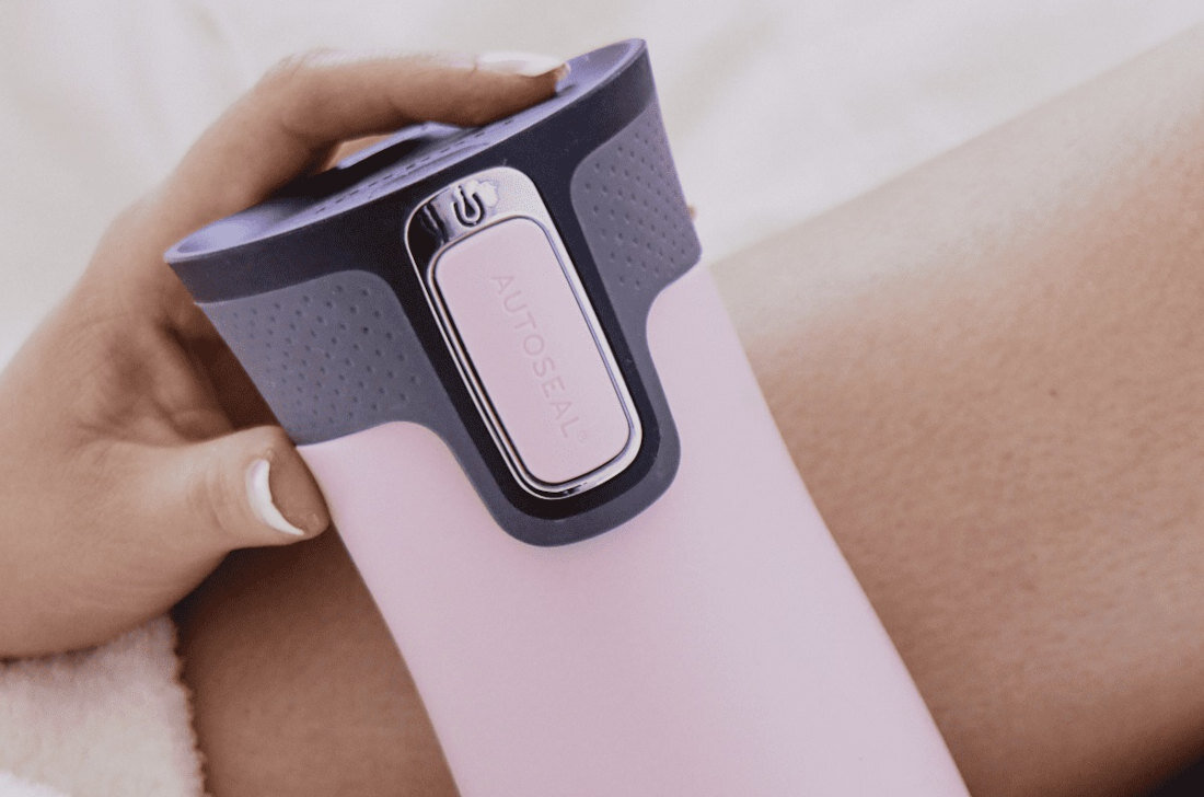 Różowy kubek termiczny z szarym wieczkiem, na którym widoczny jest przycisk z napisem \'AUTOSEAL\'.