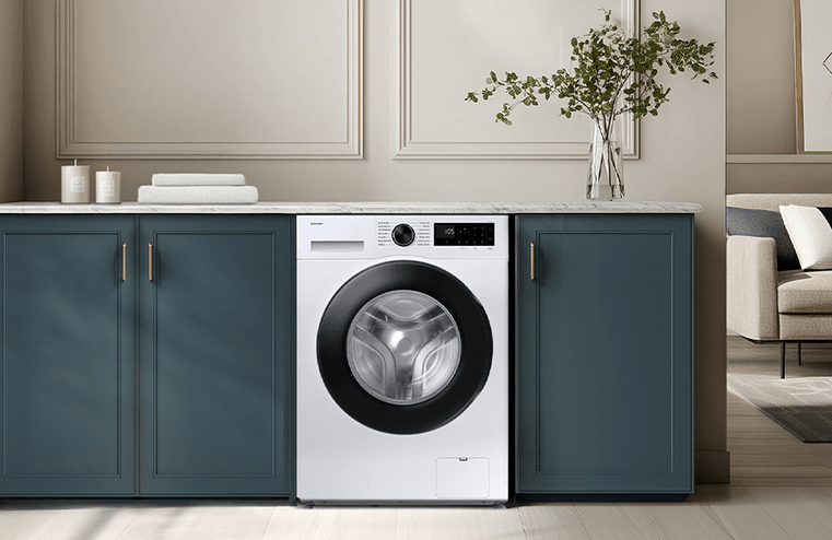 Pralka w zabudowie kuchennej z białym frontem i czarnym bębnem, otoczona szafkami w kolorze ciemnoniebieskim. Na blacie znajduje się wazon z zielonymi gałązkami oraz kilka złożonych ręczników.