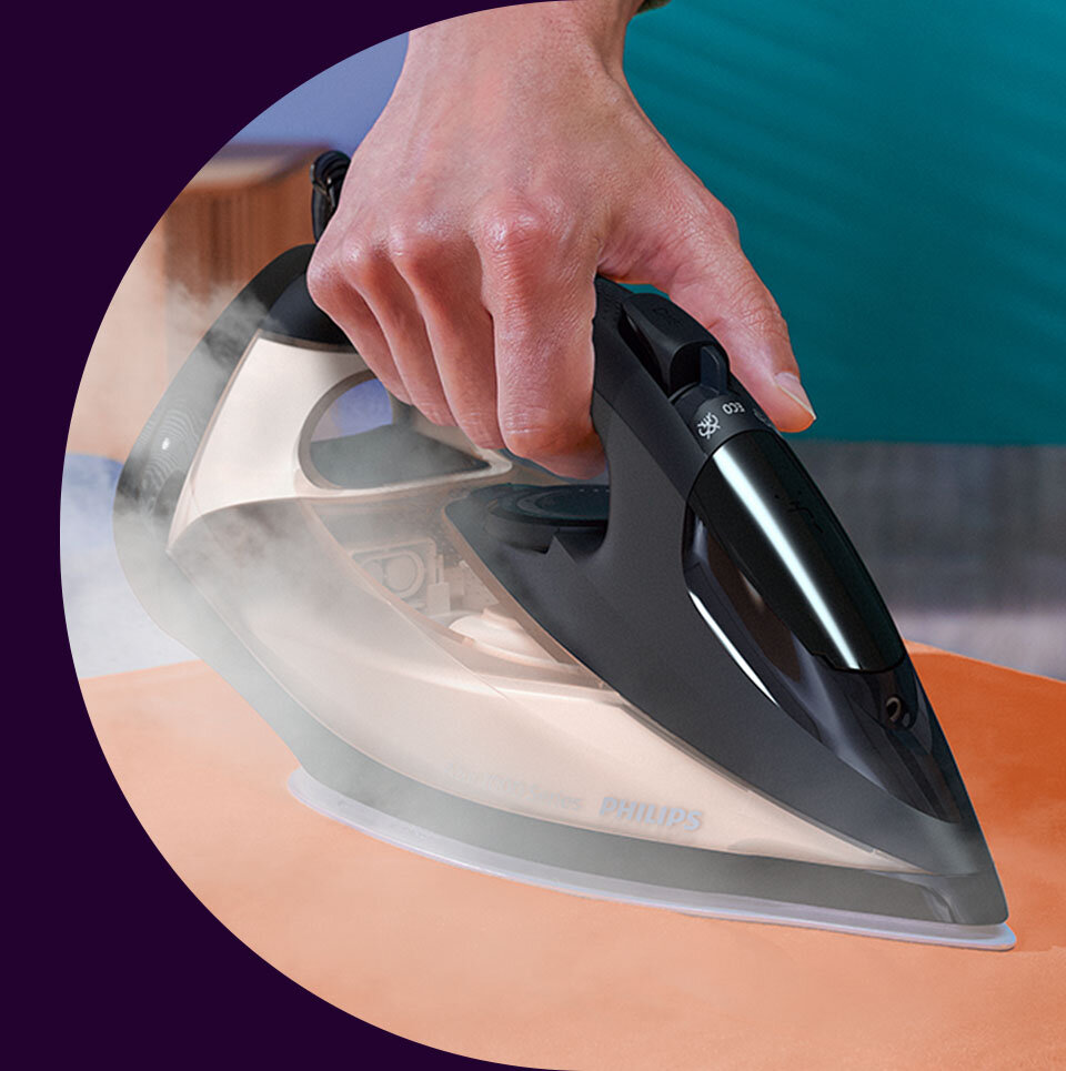 Osoba prasuje pomarańczowy materiał żelazkiem z widocznym logo \'philips\'. Z żelazka wydobywa się para.