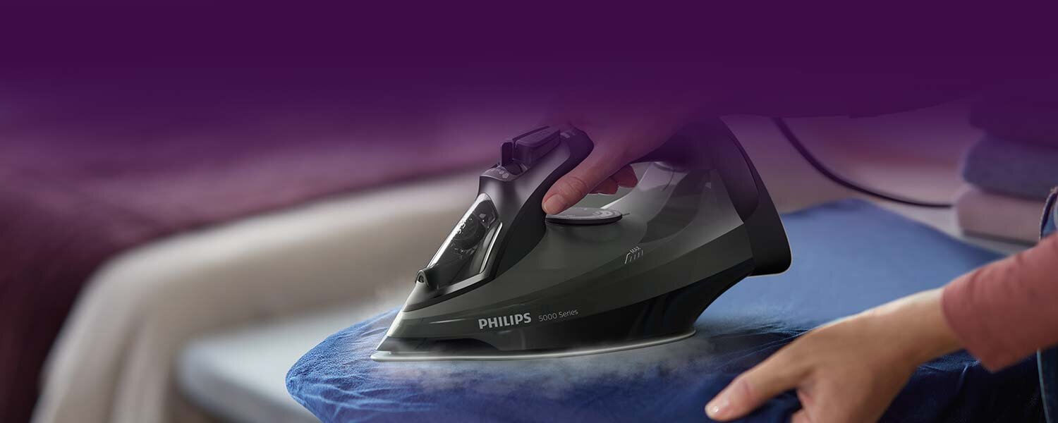 Osoba prasuje niebieski materiał żelazkiem z widocznym napisem \'PHILIPS 5000 Series\'.