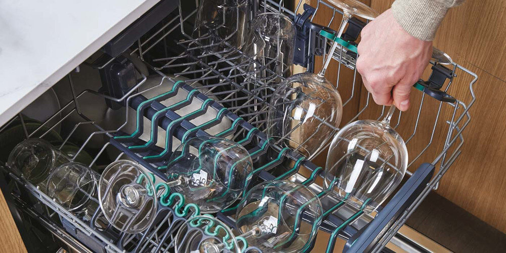 Wnętrze zmywarki z widocznymi kieliszkami umieszczonymi w górnym koszu. Osoba trzyma jeden z kieliszków, pokazując sposób ich ułożenia.
