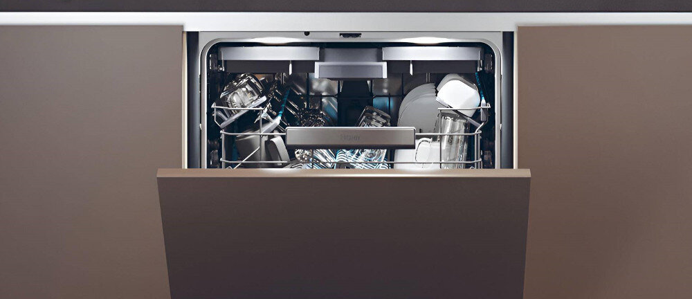 Otwarta zmywarka z widocznymi naczyniami w środku, w tym talerzami i szklankami. Wnętrze jest oświetlone, a drzwi są częściowo uchylone.