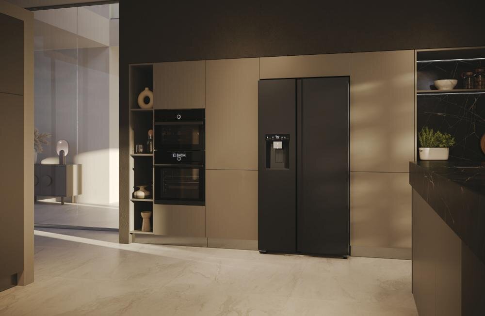 W nowoczesnej kuchni znajduje się czarna lodówka typu Side by Side z panelem sterowania i dystrybutorem wody. Obok lodówki w zabudowie umieszczono piekarnik i mikrofalówkę.