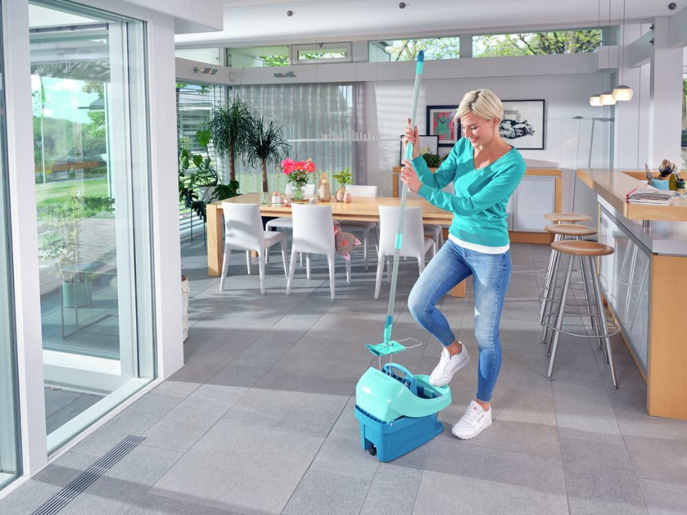 Osoba używa zestawu z mopem w jasnym, nowoczesnym wnętrzu z dużymi oknami i drewnianymi meblami. Na stole znajdują się kwiaty i dekoracje.