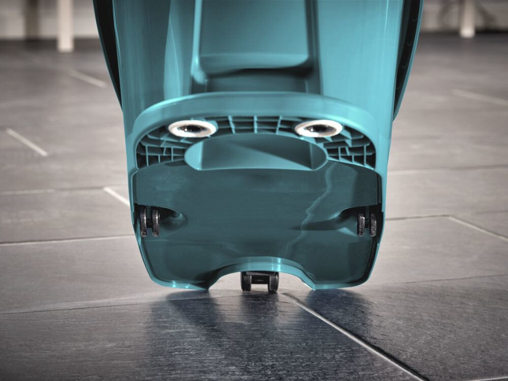 Na obrazie widoczny jest dolny fragment plastikowego wiadra w kolorze turkusowym z dwoma kółkami. Wiadro stoi na ciemnej, kafelkowej podłodze.