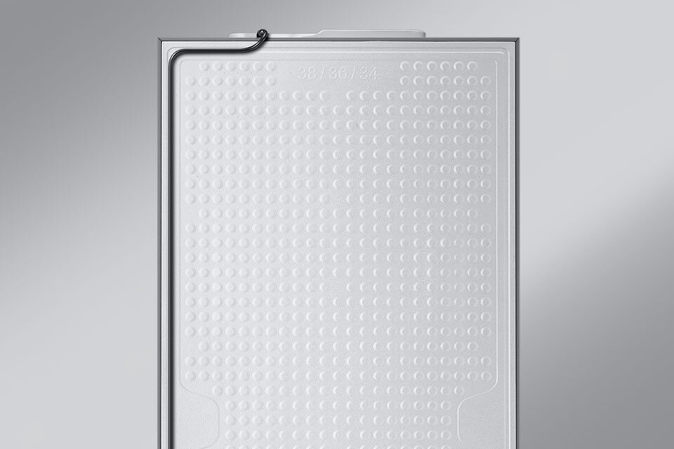 Obraz przedstawia wewnętrzną część drzwi lodówki z widoczną strukturą w postaci wypukłych kropek. Na górze widoczny jest cienki przewód oraz oznaczenie \'38/36/34\'.