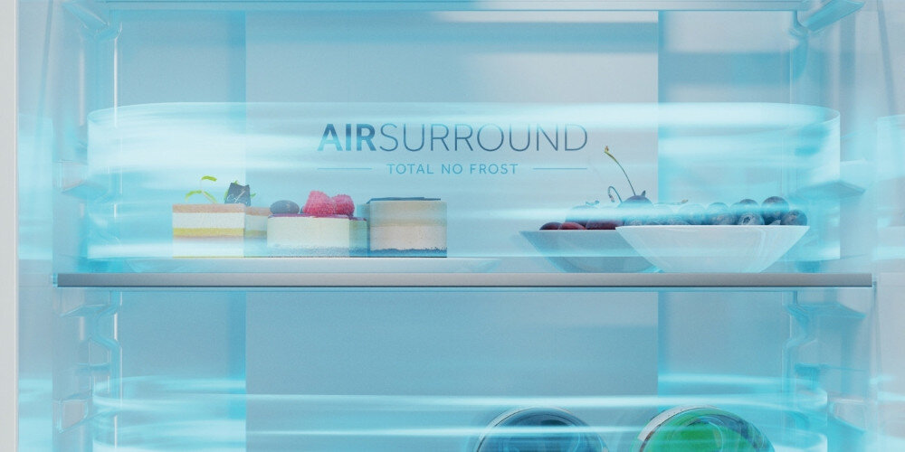 Wnętrze lodówki z widocznymi półkami, na których znajdują się ciasta i miska z owocami. Na tylnej ściance napis \'AIR SURROUND TOTAL NO FROST\'.