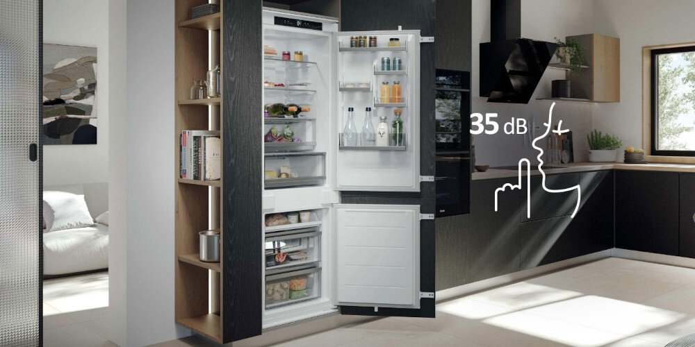 Otwarta lodówka w zabudowie kuchennej z widocznymi półkami wypełnionymi produktami spożywczymi. Obok lodówki znajduje się grafika z napisem \'35 dB\'.