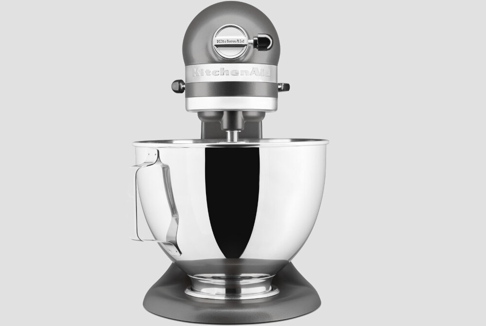 Na obrazie widoczny jest srebrny robot kuchenny z dużą metalową misą. Na górnej części urządzenia znajduje się logo \'KitchenAid\'.