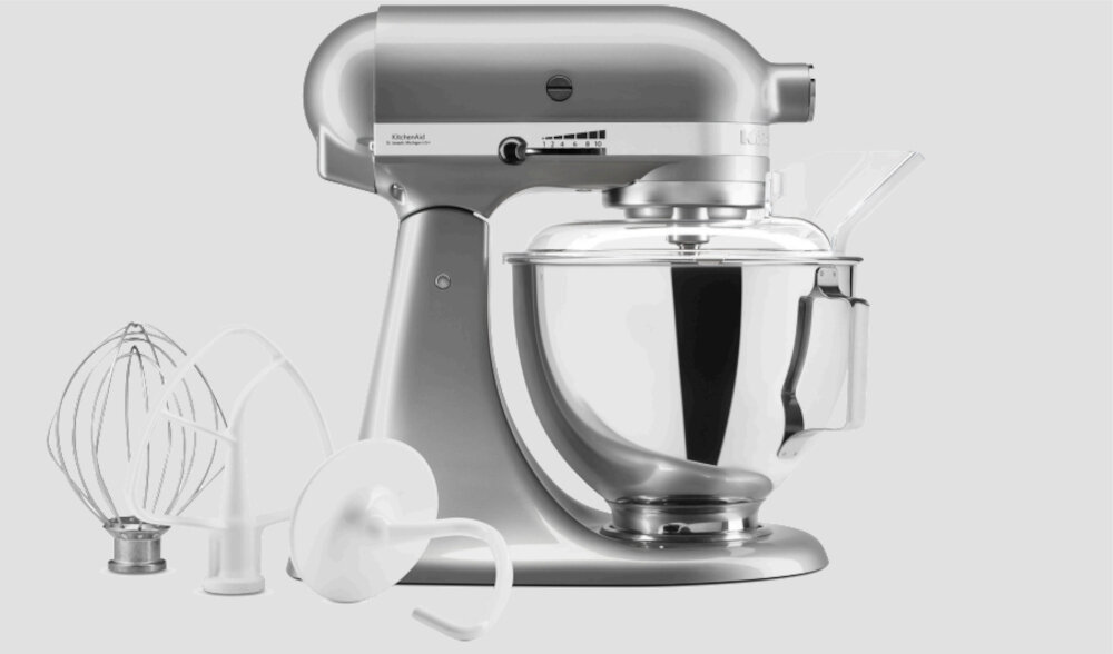 Srebrny robot kuchenny planetarny z misą ze stali nierdzewnej oraz trzema końcówkami: trzepaczką, hakiem do ciasta i mieszadłem. Na obudowie widoczne jest logo producenta oraz panel z przełącznikiem prędkości.