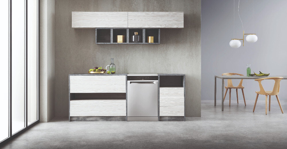 Nowoczesna kuchnia z zabudowaną zmywarką o stalowym wykończeniu, otoczona szafkami w jasnym drewnie. W tle znajduje się stół z dwoma krzesłami i wiszącymi lampami.