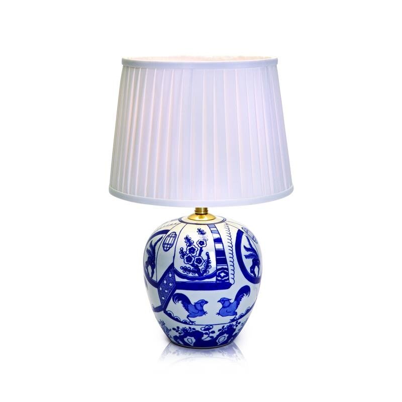 Lampa stołowa z białym, plisowanym abażurem i ozdobną, niebiesko-białą podstawą z motywami roślinnymi i zwierzęcymi.