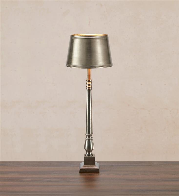 Metalowa lampa stołowa o eleganckim designie, umieszczona na drewnianym blacie, z jasnym tłem w tle.