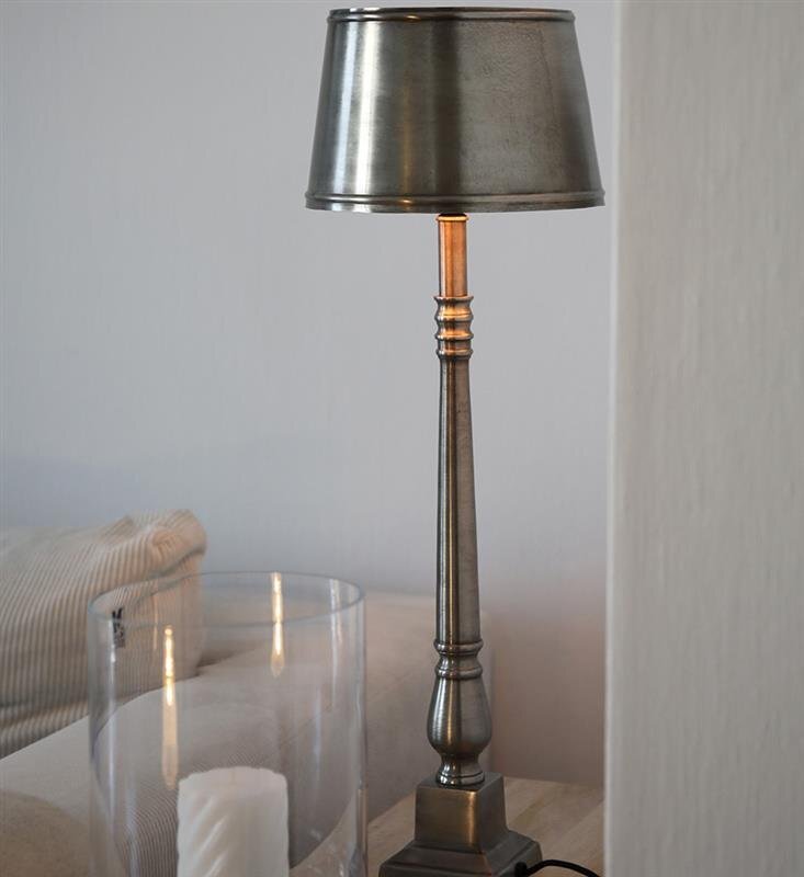 Metalowa lampa stołowa o eleganckim designie stoi na drewnianym stole obok szklanego świecznika z białą świecą.
