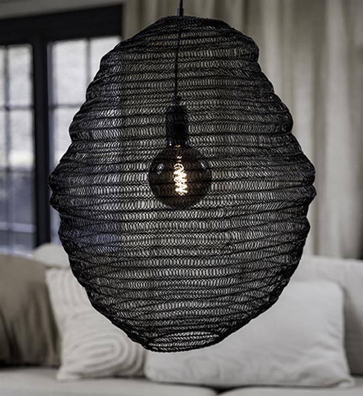 Czarna lampa wisząca o ażurowej strukturze z widoczną żarówką wewnątrz, zawieszona w pomieszczeniu z sofą i zasłonami w tle.