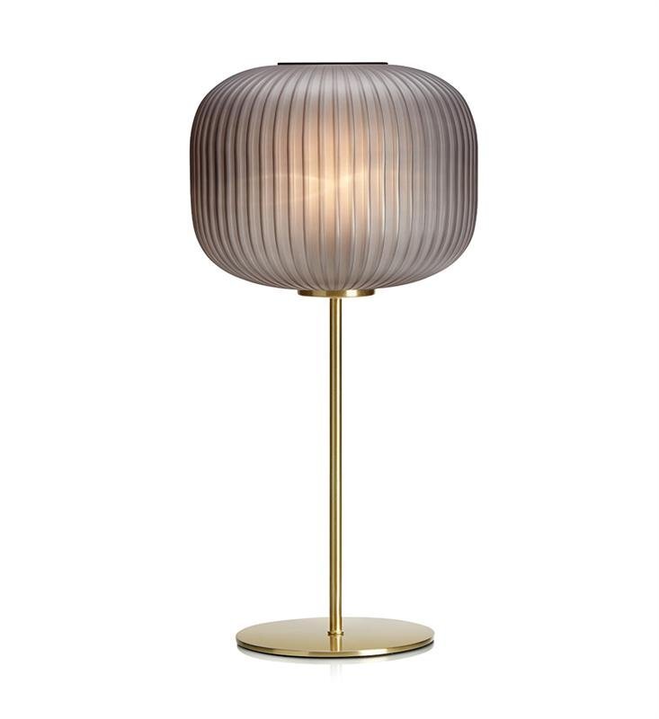 Lampa stołowa z przezroczystym, żebrowanym kloszem i złotą podstawą na białym tle.