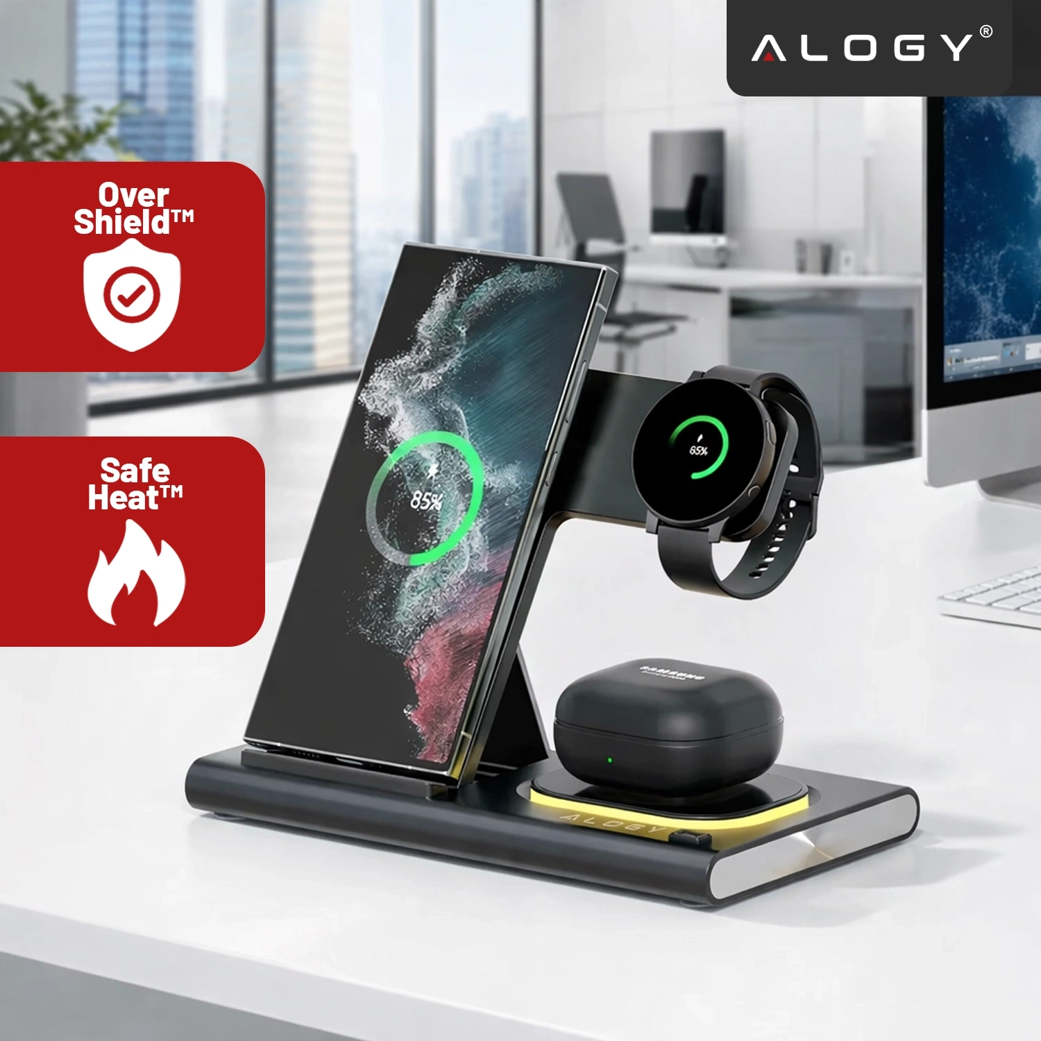 Na biurku znajduje się czarna ładowarka indukcyjna 3w1 z telefonem, zegarkiem i słuchawkami. Widoczne są napisy: \'Over Shield™\', \'Safe Heat™\' oraz logo \'ALOGY\'.