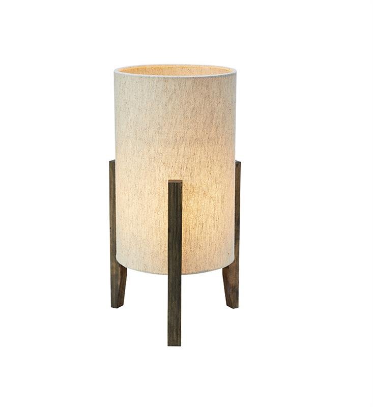 Lampa stołowa nocna z cylindrycznym abażurem w jasnym kolorze, wsparta na trzech drewnianych nogach.