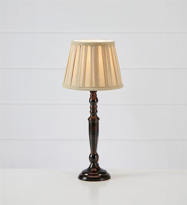 Lampa stołowa z ciemnym, eleganckim trzonkiem i beżowym abażurem, ustawiona na jasnym tle.