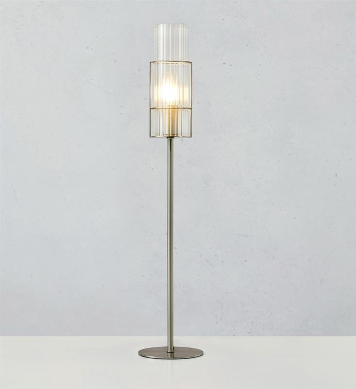 Lampa stołowa z metalową podstawą i szklanym kloszem, emitująca ciepłe światło. Tło jest jednolite, jasnoszare.