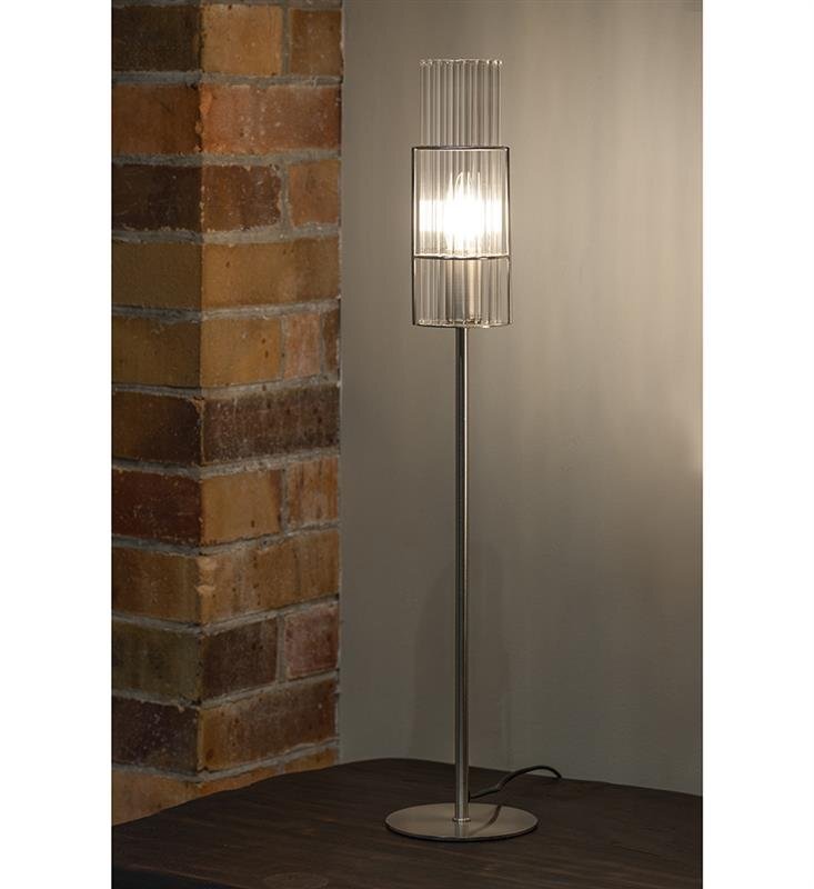 Lampa stołowa z metalowym stelażem i szklanym kloszem, emitująca jasne światło. Ustawiona na ciemnym blacie, obok ściany z cegieł.